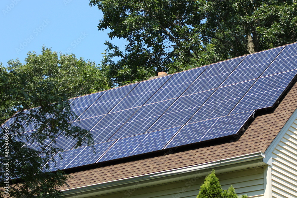 Solar panels on top of a house roof on a sunny summer day with blue sky and trees in the background Solar panels on top of a house roof on a sunny summer day with blue sky and trees in the background