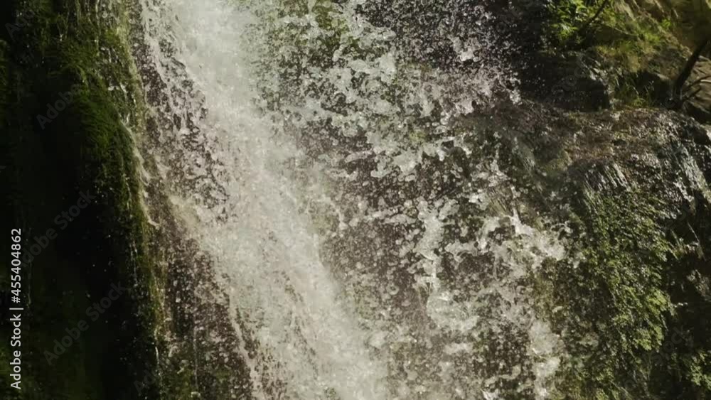 Magical mountain waterfall, crystal water, large stones overgrown with moss. The waterfall with the crystal clear water that flows quickly. slow motion. 4K. B ROOL. Camera tilt down from up.