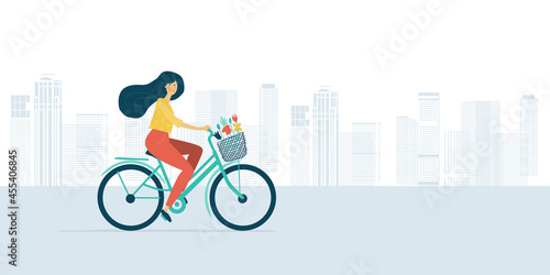 Woman riding bicycle with basket of flowers. Cityscape background