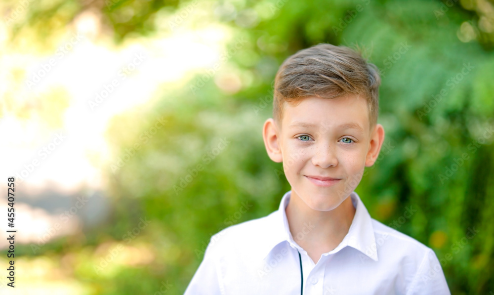 The boy is smiling against the background of blurred green trees
The boy is smiling against the background of blurred green trees