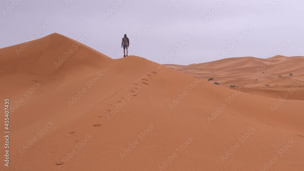 A man climb a sand dune in the Sahara desert to overlook his position, static shot A man climb a sand dune in the Sahara desert to overlook his position, static shot