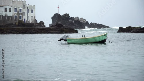 A Wooden Tealed Colored Boat Anchored Along the Rocky Coastal of San Bartolo, Lima, Peru photo