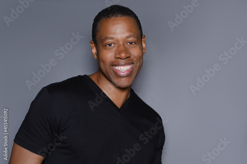 Portrait of  smiling African American man in plain black t-shirt standing in front of gray background photo