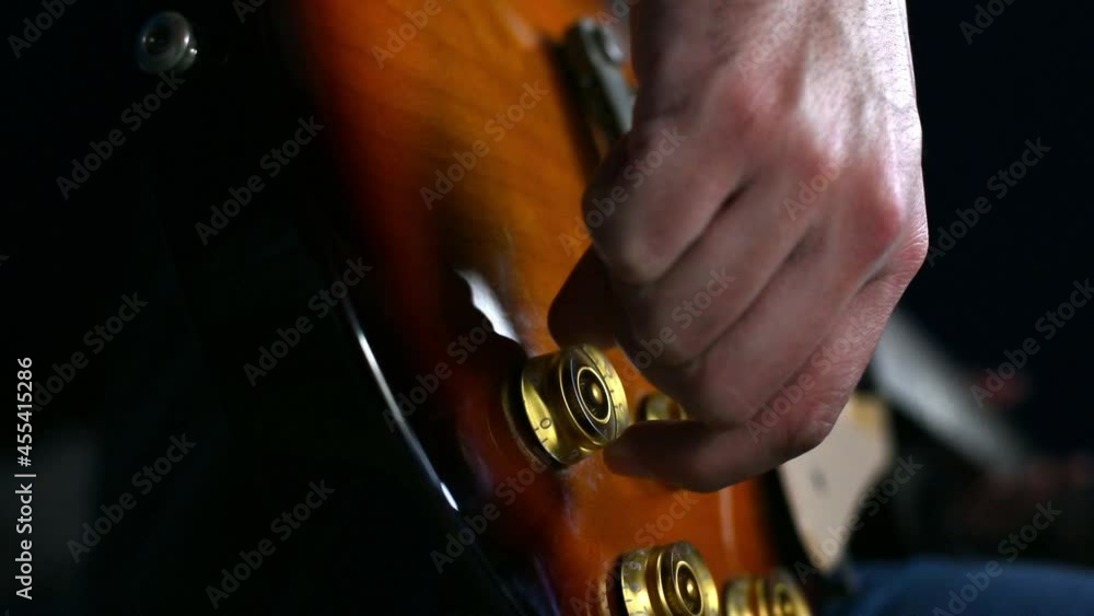 Concentrated guitarist hand rotates volume and tone control of guitar