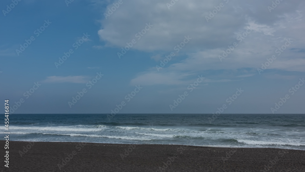 The coast of the Pacific Ocean. Surf waves foam on the black volcanic sand of the Khalaktyrsky beach. There are picturesque clouds in the blue sky. Kamchatka.
