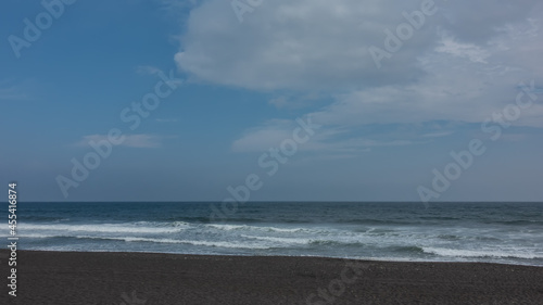 The coast of the Pacific Ocean. Surf waves foam on the black volcanic sand of the Khalaktyrsky beach. There are picturesque clouds in the blue sky. Kamchatka.