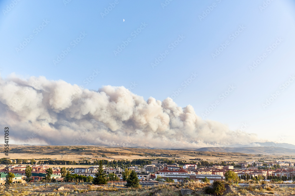Obraz premium Photograph of a large forest fire with a large column of smoke on a hillside near a city