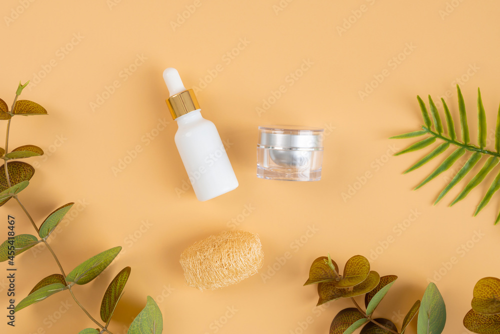 White bottle cosmetic products and green leaves on orange background.