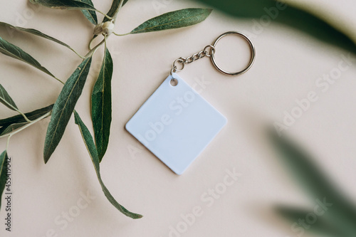 Keychain mockup among olive leaves to display design. Blank white sublimation key chain photo. photo