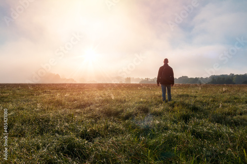 Young caucasian man standing, walking on meadow in misty fog at sunrise. Czech summer landscape