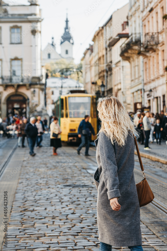 Woman in a coat is walking down the street of rynok square in old city center of Lviv.