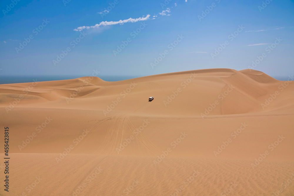 A white jeep driving in the yellow sand dunes. The Namib Desert on the Atlantic coast.