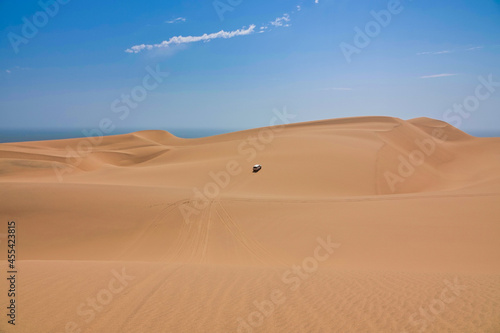 Fototapeta Naklejka Na Ścianę i Meble -  A white jeep driving in the yellow sand dunes. The Namib Desert on the Atlantic coast.