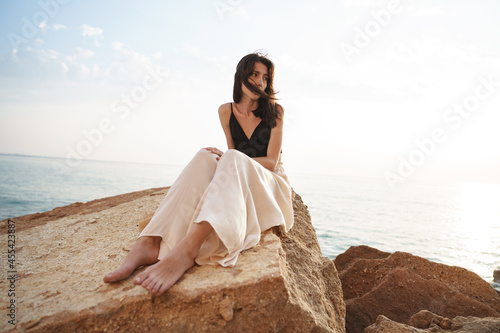 Woman traveler sitting near sea on cliff injoying view of sea and nature photo