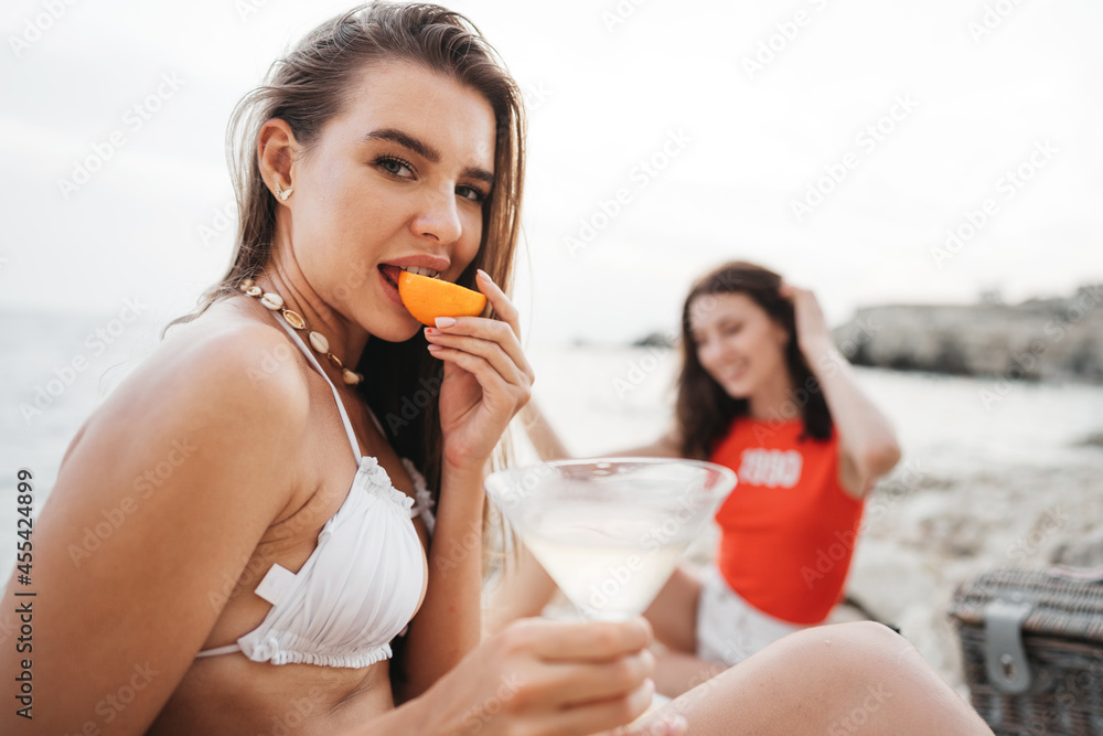 Two young female friends having picnic on a beach drinking cocktails Two young female friends having picnic on a beach drinking cocktails
