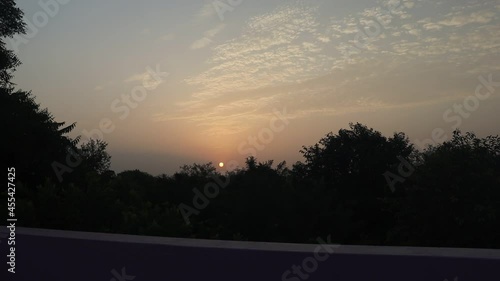time laps video of the bright sun rising from behind the hills in the scattered clouds and the silky forest trees