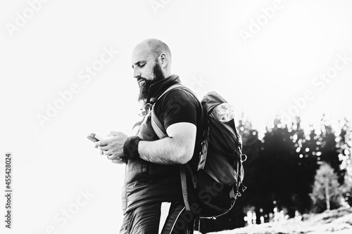 Young tourist man uses a mobile phone in the mountains. The man is looking for the right route. Black white photo. A handsome bald man with a beard travels in the mountains.