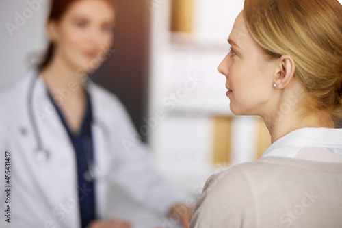 Friendly smiling female doctor and patient woman discussing current health examination in sunny clinic. Perfect medical service in hospital. Medicine concept