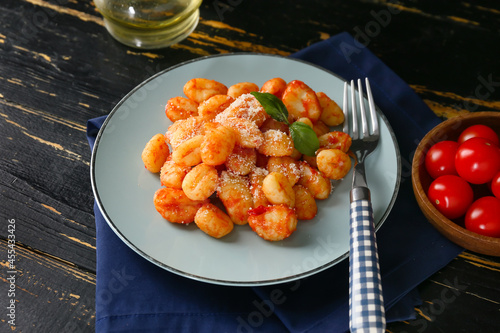 Delicious gnocchi with tomato sauce in plate on dark wooden table photo