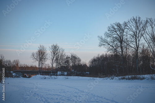 golden winter evening landscape from frozen snow and ice covered river, dry yellow reeds in distance, clear sky, copy space, footprints in snow, transport bridge further. Latvia landscape in cold