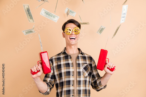 Photo of cheerful crazy guy hold pistol throw blow money wear specs plaid shirt isolated beige color background
