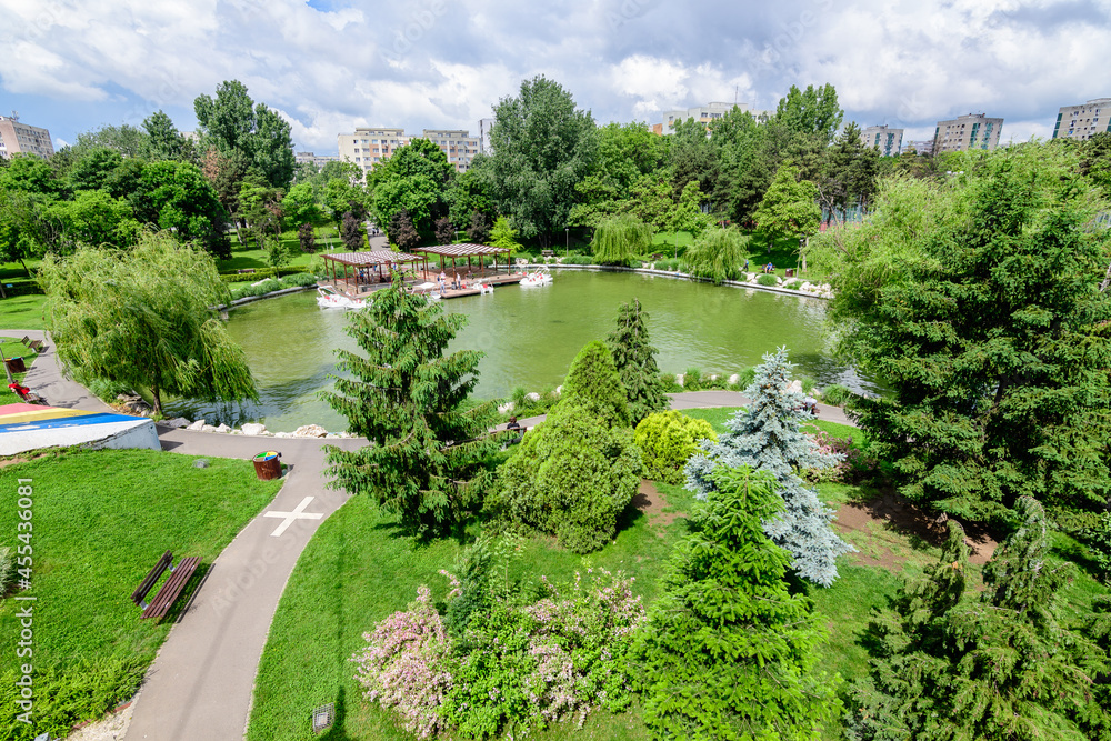 Fototapeta premium Landscape with lake and vivid green trees in Drumul Taberei Park (Parcul Drumul Taberei) also known as Moghioros Park, in Bucharest, Romania, in a cloudy summer day.