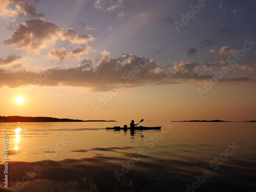 Kayaking silhouette on a calm sea far away at sunset.