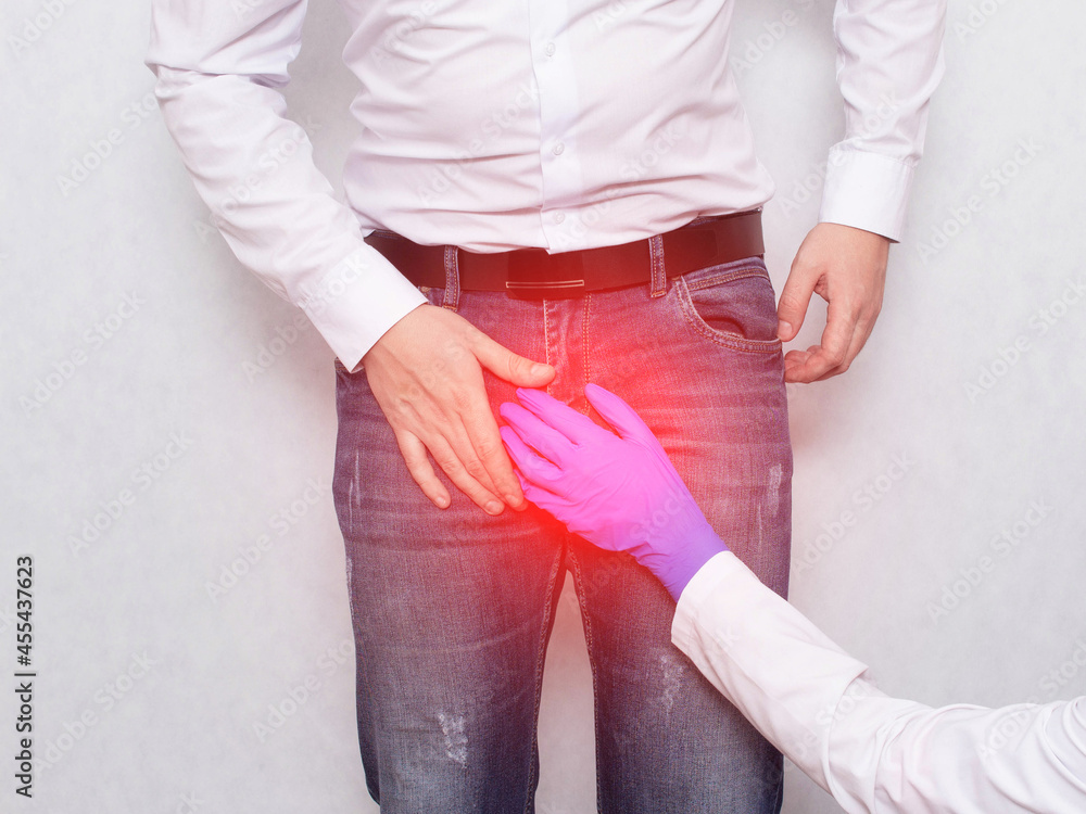 A doctor in a medical glove holds on to the groin area of a male patient.  Concept of genitourinary diseases, varicocele and prostatitis in men Stock  Photo