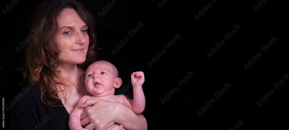 Happy woman mother holds a newborn baby boy in her arms, black studio background. Mom smiles with a child in her hands Happy woman mother holds a newborn baby boy in her arms, black studio background. Mom smiles with a child in her hands