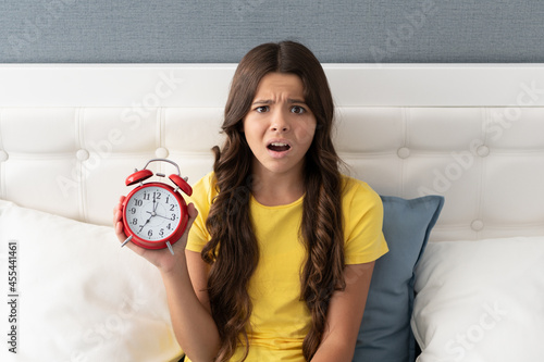Worried girl child hold alarm clock being upset with oversleeping morning, late photo