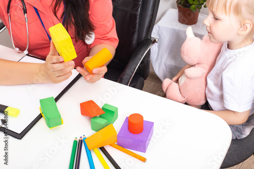 The doctor shows the multi-colored figures of the constructor to a little girl 3-4 years old. Development of thinking and logic in children, close-up photo