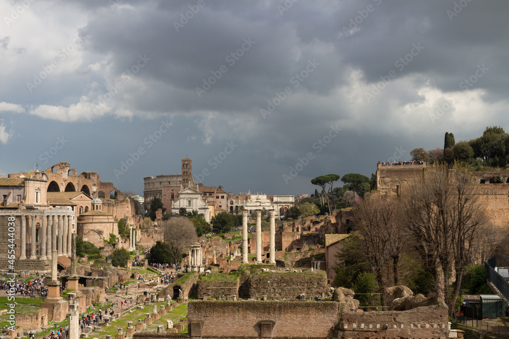 Top view of the Roman forum, illuminated by the sun, against a dramatic sky. Ancient architecture and the urban landscape of historical Rome