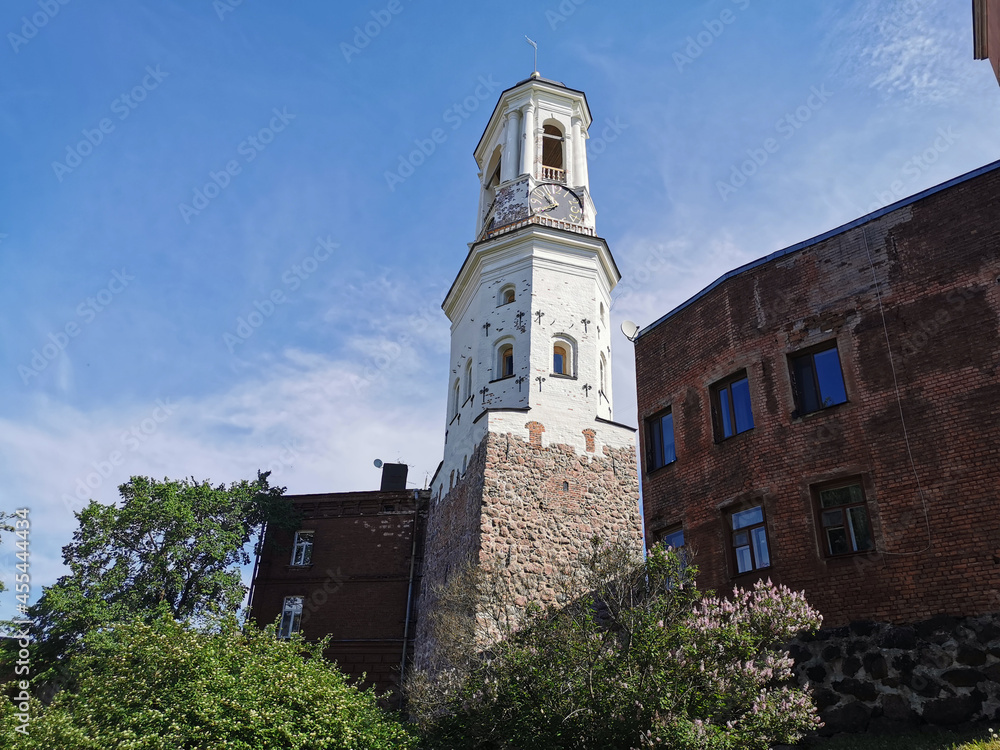 An old clock tower, a former bell tower, standing between residential buildings in the city of Vyborg on a clear summer day.