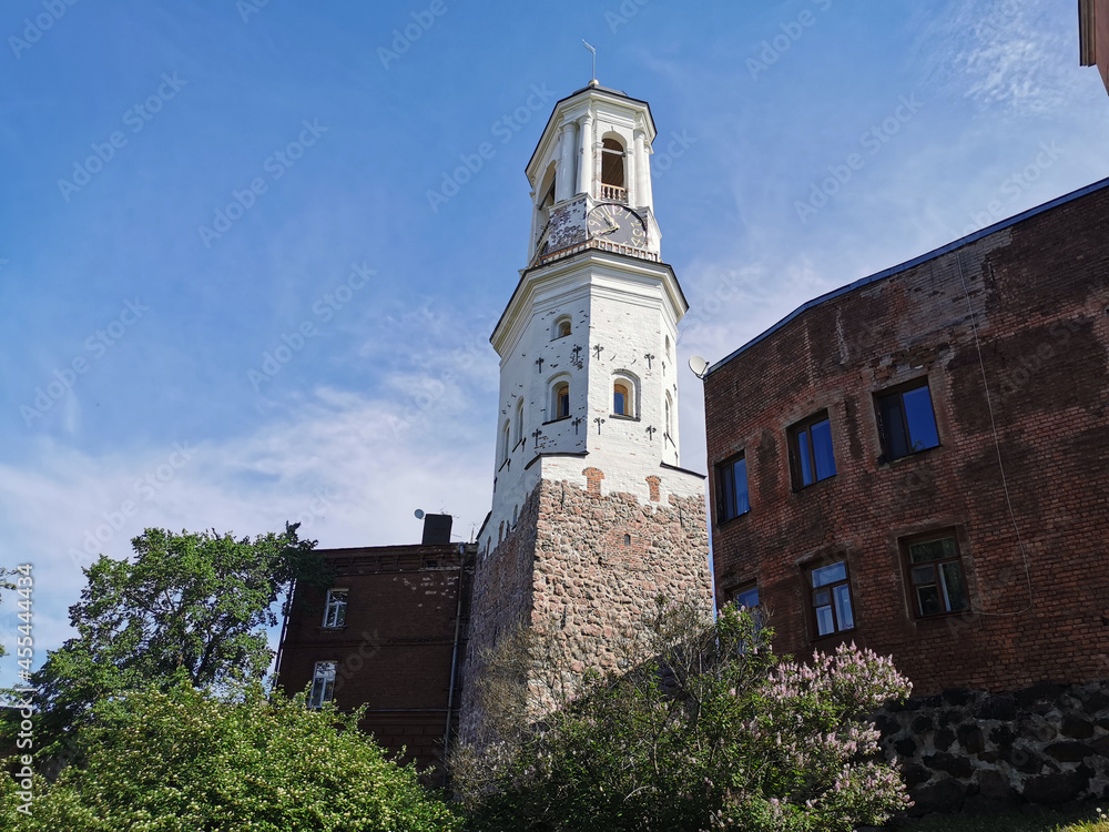 An old clock tower, a former bell tower, standing between residential buildings in the city of Vyborg on a clear summer day. An old clock tower, a former bell tower, standing between residential buildings in the city of Vyborg on a clear summer day.