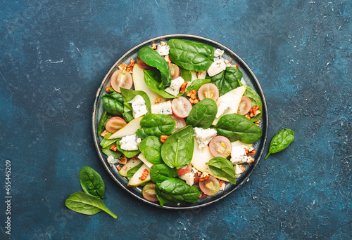 Salad with pear, blue cheese, spinach, grapes, walnuts on blue background, top view, copy space
