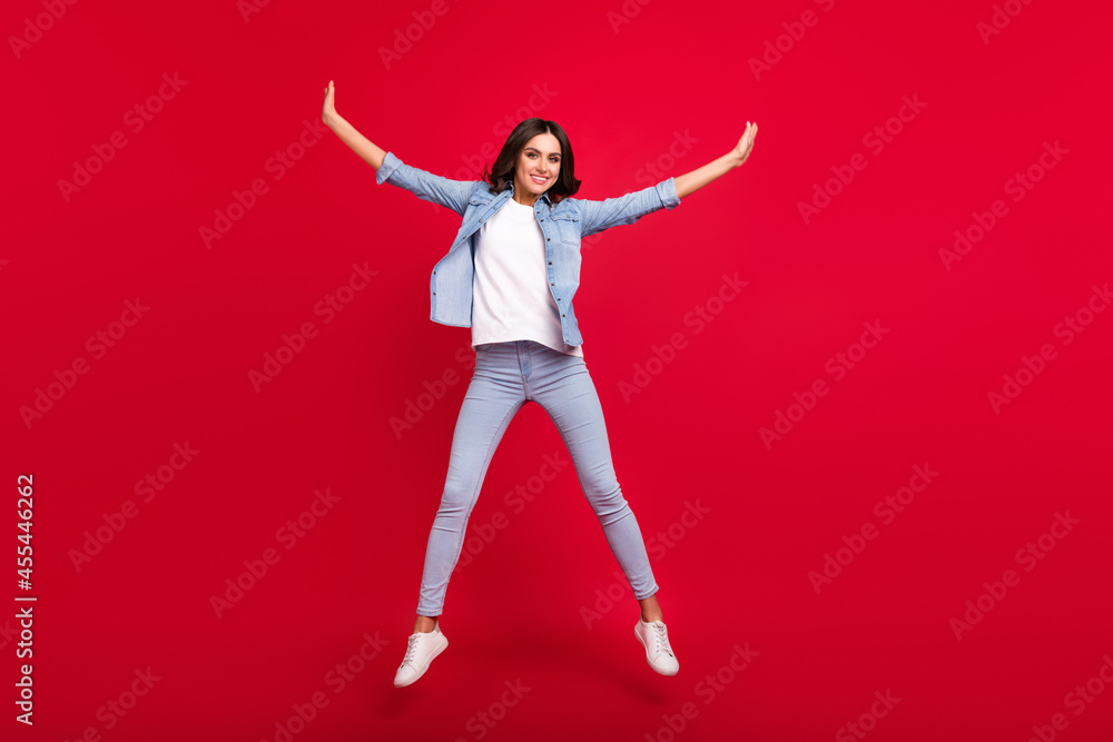 Full length body size view of attractive carefree cheerful girl jumping having fun isolated over vibrant red color background Full length body size view of attractive carefree cheerful girl jumping having fun isolated over vibrant red color background