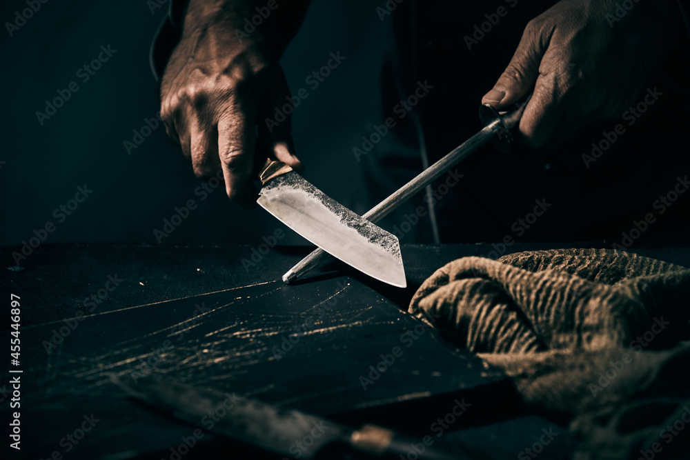 Chef sharpening a large knife on a handheld metal file StockFoto