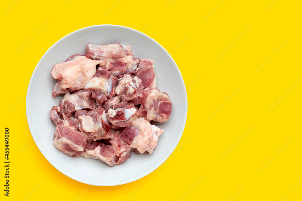 Raw pork ribs in white plate on yellow background.