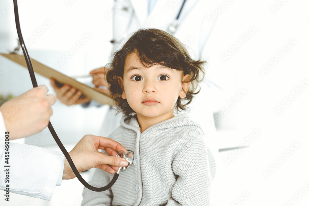 Woman-doctor examining a child patient by stethoscope. Cute arab toddler at physician appointment. Medicine concept Woman-doctor examining a child patient by stethoscope. Cute arab toddler at physician appointment. Medicine concept