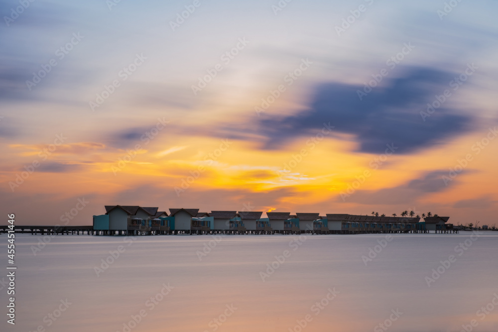 Beautiful vivid sunrise over beach with the villas in the Indian ocean, Maldives, South Male atoll. July 2021. Long exposure picture