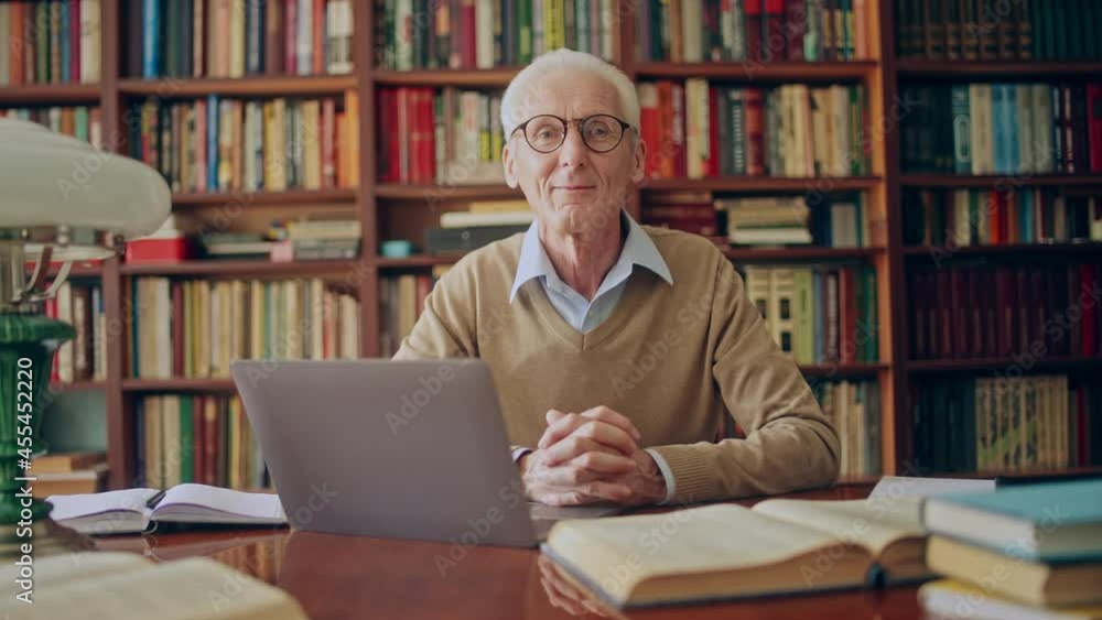 Portrait of friendly senior man working on laptop in library, doing research Portrait of friendly senior man working on laptop in library, doing research