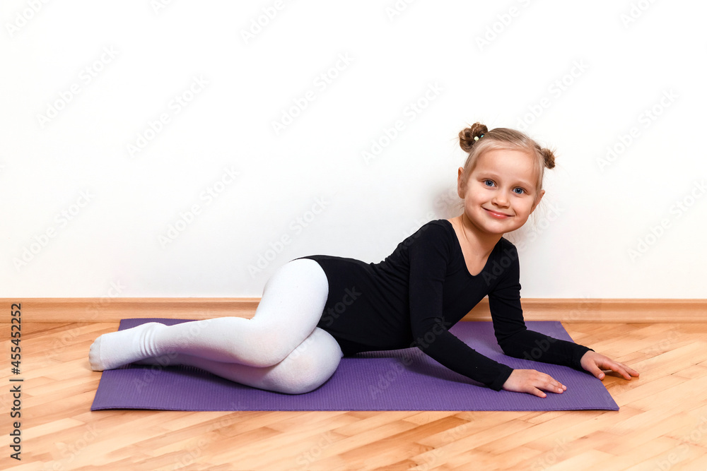 Athletic child rests on a mat after home training. Little girl in a black leotard lies on the floor Athletic child rests on a mat after home training. Little girl in a black leotard lies on the floor