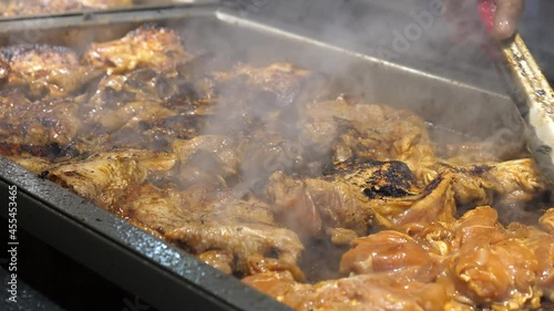 Close up view of chef's hand moving steaming cooking pieces of Jamaican jerk chicken with kitchen tongs at take away or takeout stall. photo