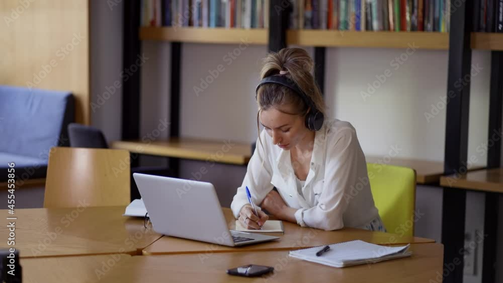 Blonde woman study at distant learning at library, taking notes Blonde woman study at distant learning at library, taking notes