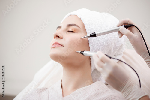 Young woman having micro current galvanic facial treatment with electrodes for lifting face. Concept preventing acne and oily skin problems photo
