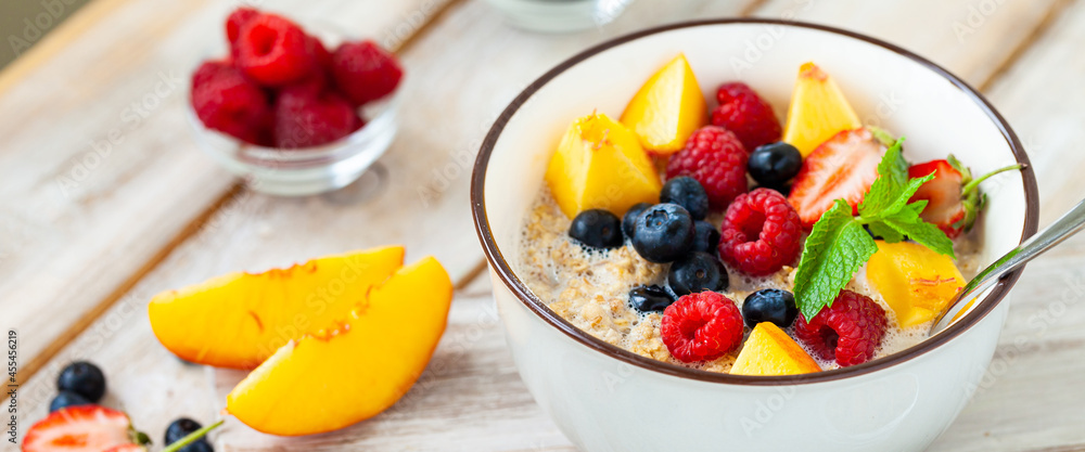 Bowl with vegan granola with fresh ripe organic berries, peach, plant milk, mint. Concept of dieting, detox, tasty simple super food, healthy low calories breakfast. Wooden background, close up banner Bowl with vegan granola with fresh ripe organic berries, peach, plant milk, mint. Concept of dieting, detox, tasty simple super food, healthy low calories breakfast. Wooden background, close up banner