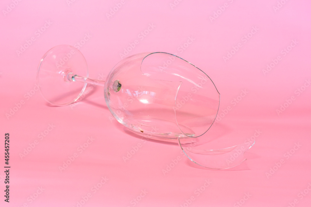 broken wine glass with shards on pink background