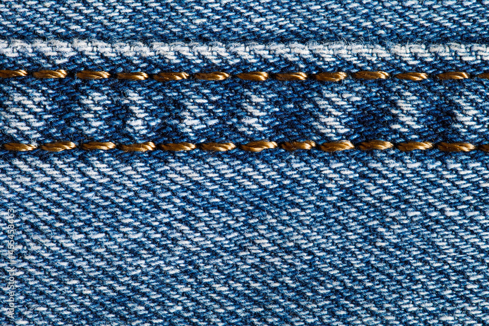 Denim fabric, background structure, stitched stitch with gold threads, close-up macro view Denim fabric, background structure, stitched stitch with gold threads, close-up macro view