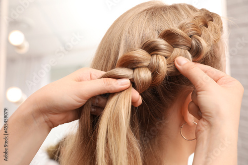 Фотография Professional stylist braiding client's hair in salon, closeup