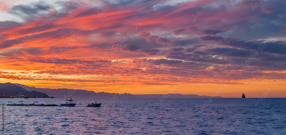Colorful clouds during sunrise above sea and mountains